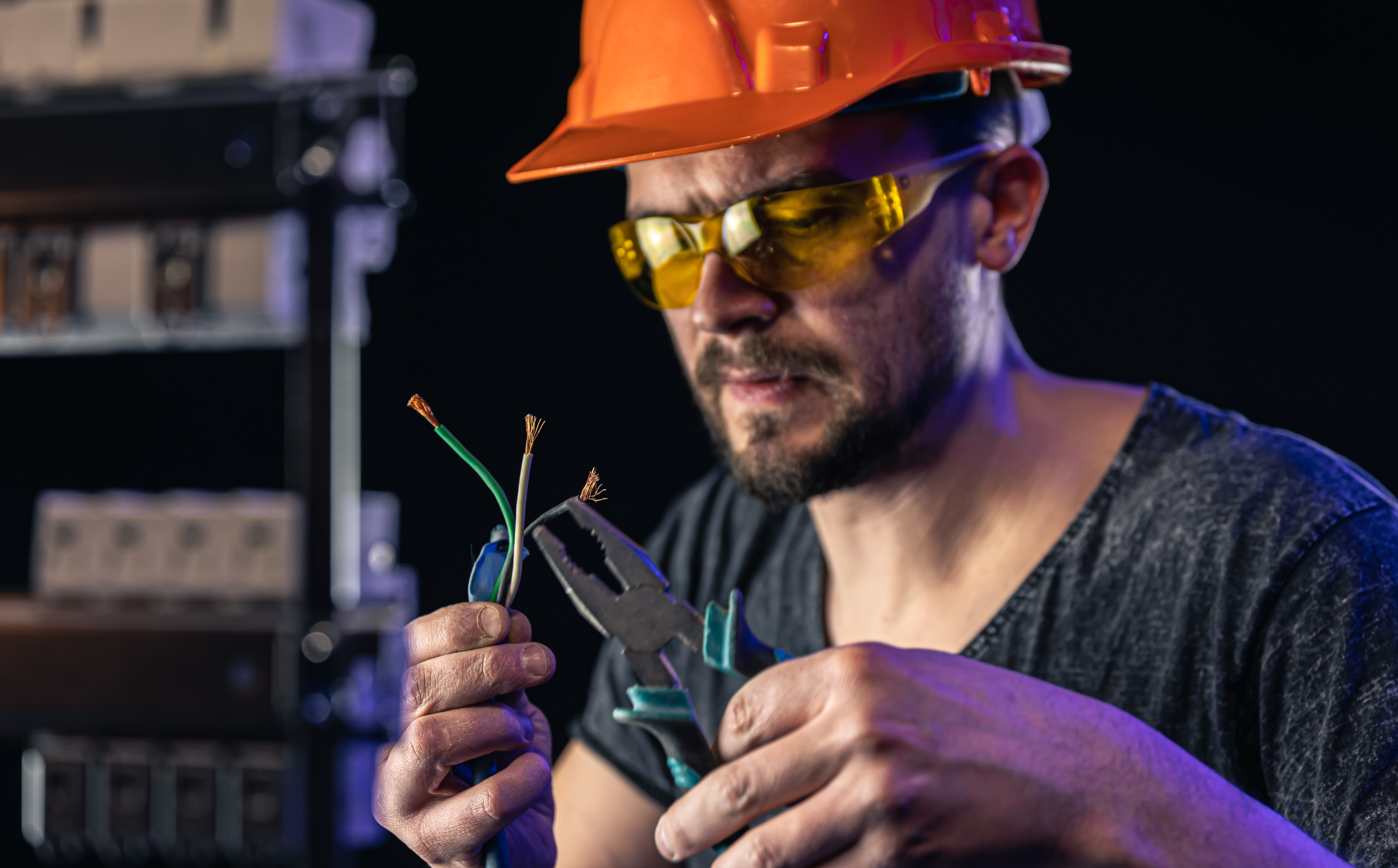 A male electrician works in a switchboard with an electrical connecting cable.